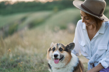 Outdoors portrait of funny cute Welsh Corgi dog and young beautiful woman together amidst the scenic lawn