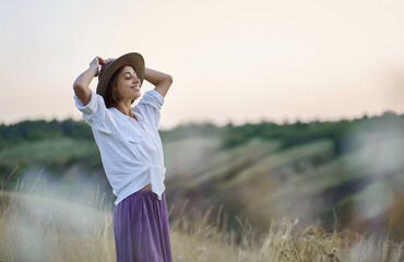 Graceful woman in beautiful nature with serene hillside walking in meadow during sunset