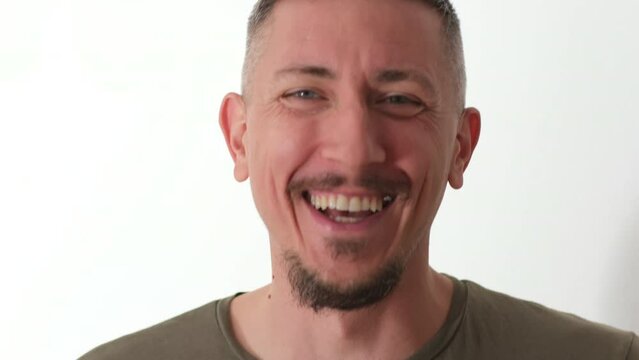 The face of a rejoicing man close-up on a white background. A handsome man with a mustache and goatee shows emotions of delight and joy. Happy man, slow motion, close-up portrait. Emotional 4K video.