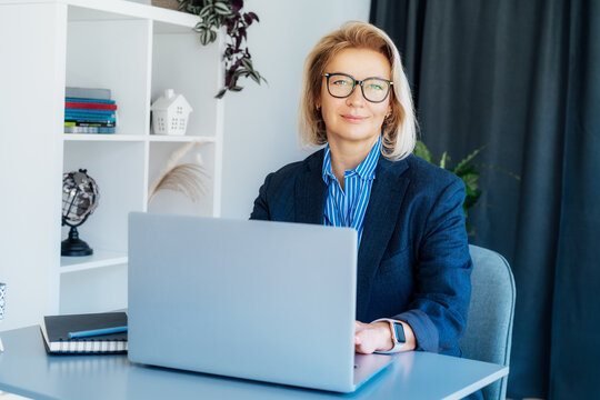 Portrait of smiling 50's stylish, confident mature businesswoman, middle aged company ceo director, experienced senior female professional, business coach working on laptop in office. Female leader