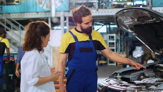 Experienced mechanic in auto repair shop showing customer malfunctions found inside car after thorough inspection. Repairman telling woman vehicle diagnostic after checking for broken parts