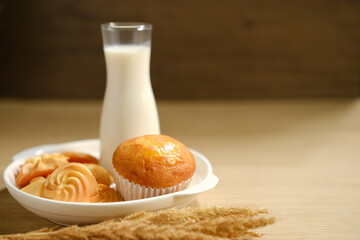 homemade muffins in white paper muffin cups and cookies a glass of milk on the table.