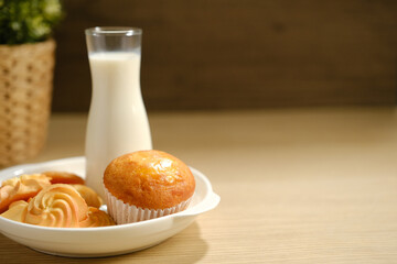homemade muffins in white paper muffin cups and cookies a glass of milk on the table.