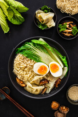 Gyoza ramen - broth with traditional Japanese dumplings filled with vegetables wrapped into thin dough, noodles boiled eggs and vegetables on wooden table
