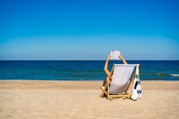 Woman relaxing on beach reading book sitting on sunbed
