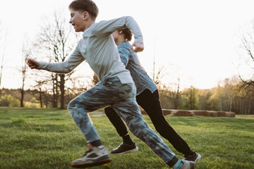 Two energetic teenage boys running across meadow at sunset, playing football together and enjoying active leisure. © Евгения Рубцова