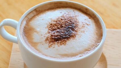 Hot cappuccino on wooden table, creamy froth, rich aroma, brown espresso, milk swirl, morning coffee delight. Steaming cappuccino in a cozy cafe setting