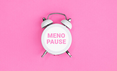 White vintage alarm clock with an inscription MENOPAUSE on pink background.