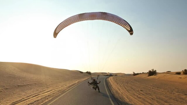 Flying directly behind paramotor over desert road - Sunrise
