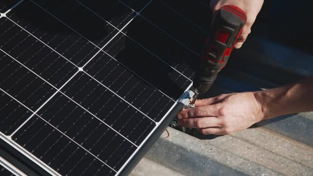 Workers installing solar panels on a metal stand, close-up. Close up of manual installation of photovoltaic solar panels on the roof of a house. Engineers work outdoors.