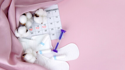 Women's menstrual pads, tampons, female menstruation calendar and alarm clock on a pink background.