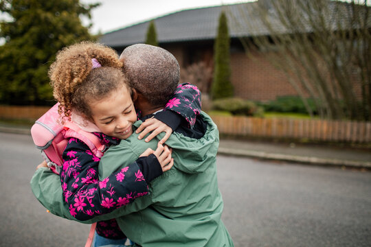 Young African American father greeting his daughter after school on the drive way of their house