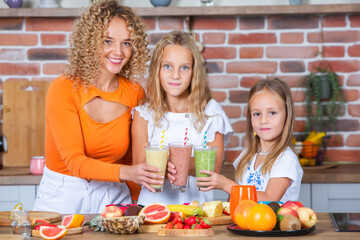 Mother and daughters cooking together in the kitchen. Healthy food concept. Portrait of happy family with fresh smoothies. Happy sisters.