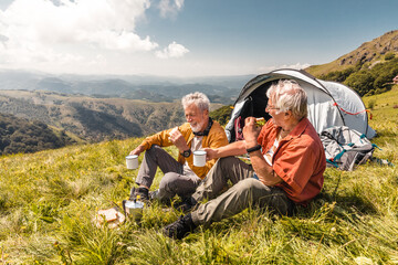 Two senior male friends having lunch while camping in the forest and mountains