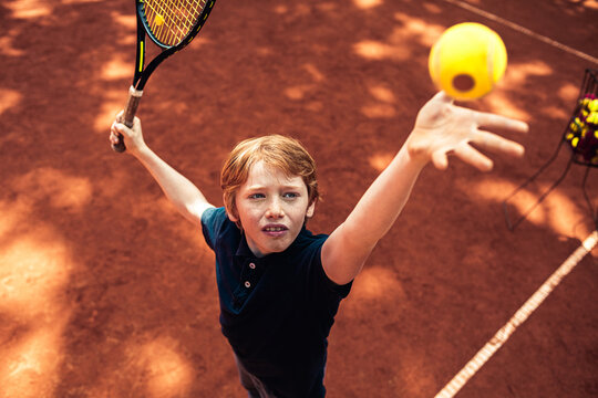 Young Caucasian boy practicing his tennis serve on a outdoor clay court