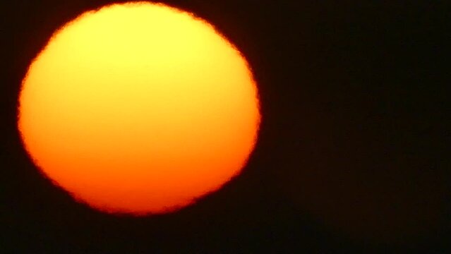 Dark sky with red and yellow solar disk with Atmospheric refraction during sunrise and flying birds. Sun with distorted shape caused by atmospheric optical phenomenon - real time. 