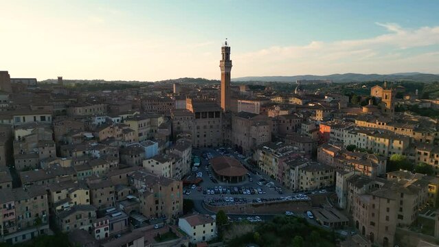 Aerial of the Torre del Mangia (Mangia Tower) and the rooftops of Siena, Italy. Duomo di Siena is in the background, track in, flying low