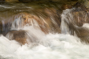 Mountain stream crashing over river rocks with white water and brown hue stones