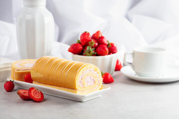 Fototapeta na wymiar Delicious biscuit roll cake with fresh strawberries on a white stone table.