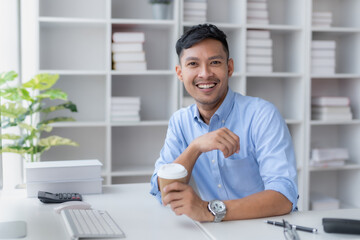 Happy smiling Asian businessman holding a coffee mug sitting happily in the office.