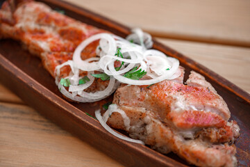 Grilled pork meat with onions on wooden stand, selective focus, side view