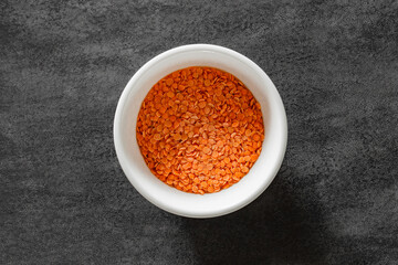 Red lentils raw, grains in bulk on white bowl, on dark background, top view, space to copy text.