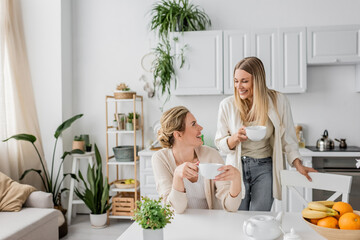 beautiful lovely sisters smiling and looking at each other on kitchen backdrop, family bonding