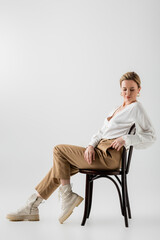 stylish blonde woman in stylish formal attire sitting on chair and relaxing, style and fashion