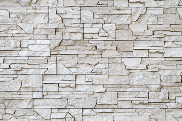 Wall, masonry of flat chipped stones beige split uneven convex, close-up, uniform texture background