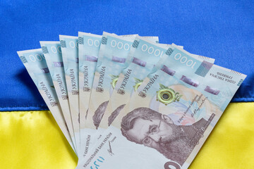 one thousand Ukrainian hrivnya banknotes lying on fabric Ukrainian flag