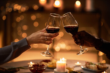 Close up of two people clinking wine glasses at dinner table with Christmas lights in background,...