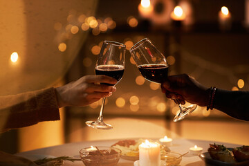 Close up of two people toasting with wine glasses at dinner table with Christmas lights in...
