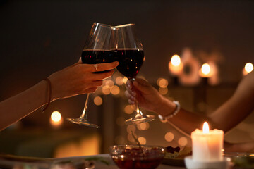 Close up of two young women toasting with wine glasses at dinner table with Christmas lights, copy...