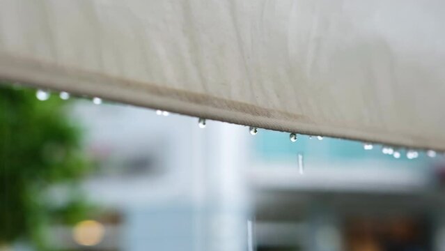 Rainy weather, summer day, drops fall from the edge of the awning on the street area in a cafe. Drops fall from the edge of the awning, shot in close-up.