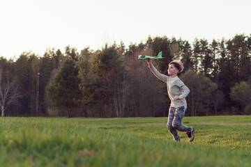 Gorgeous teenage boy running across meadow, keeping arm up and playing with toy plane, enjoying adventure in nature.