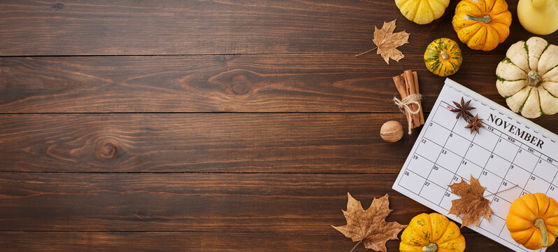 Creating a Thanksgiving mood on 23th November. Top view composition of calendar, ripe pumpkins, cinnamon sticks, autumn leaves, anise on wooden background with advert zone