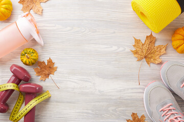 Fall season strength training. Top view photo of trendy sneakers, tape measure, dumbbells, plastic bottle, karemat, pumpkin, fallen leaves on light wooden background with ad zone