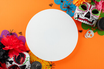 Celebrate the vibrant culture of Dia de los Muertos. Top view flat lay of carnival masks, candles, flowers, paper garland, scary elements on orange background with blank circle for advert or text