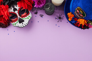 Mexican Culture and Day of the Dead concept. Top view shot of traditional masks, blue hat, candles, flowers, confetti, spooky decorations on soft purple background with advert area