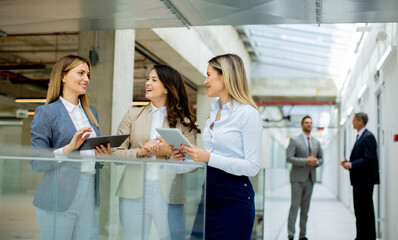 Three young business women with digital tablets discussing business ideas in the office hallway