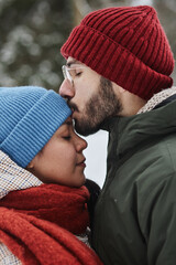 Side view closeup of young couple outdoors in winter with man kissing girlfriend gently on forehead