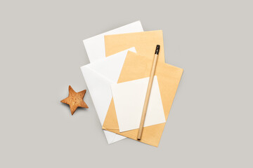 Sobres y papeles en blanco apilados junto a un lápiz de madera y una estrella marrón de madera sobre un fondo gris claro aislado. Vista superior y de cerca. Copy space