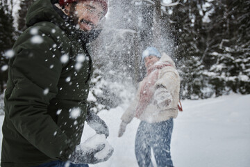 Fototapeta premium Portrait of happy young couple throwing snowballs outdoors in winter and having fun, copy space