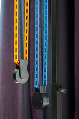 Manual mounting support system with two blue and yellow chains for cross bars and rolls of paper backgrounds for photo studio hangs, front view, close up.