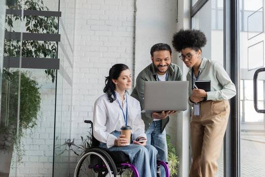 group shot of diverse business people, disabled woman on wheelchair looking at laptop with coworkers