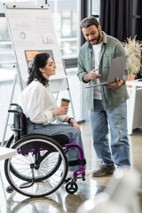 indian man showing startup project on laptop to disabled woman in wheelchair, inclusion concept