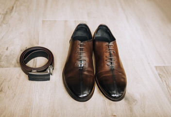 Men's brown leather stylish shoes and a black belt lie on the floor. Close-up photo, top view.