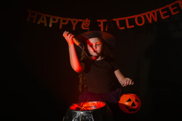 Child girl witch cooking a potion in the cauldron at halloween holidays.