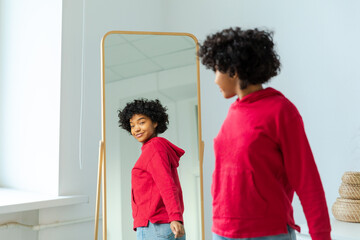 Love yourself. Beautiful young smiling african american woman dancing enjoying her mirror reflection. Black lady looking at mirror looking confident and happy. Self love concept - obrazy, fototapety, plakaty
