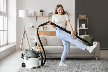 Young woman with vacuum cleaner dancing at home